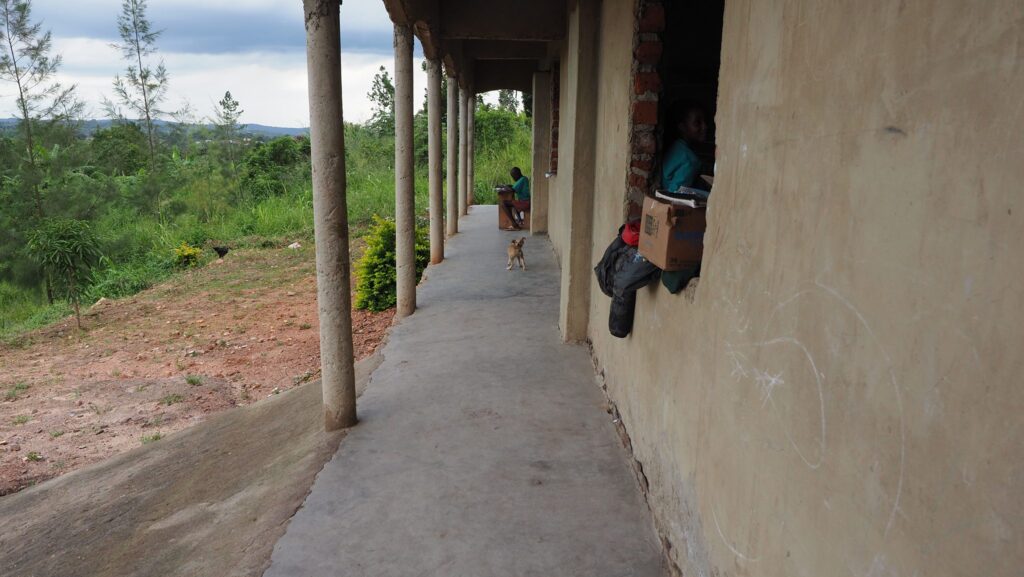 Schüler lernen im Freien auf einem überdachten Gehweg einer ländlichen Schule. Ein kleiner Hund läuft vorbei.