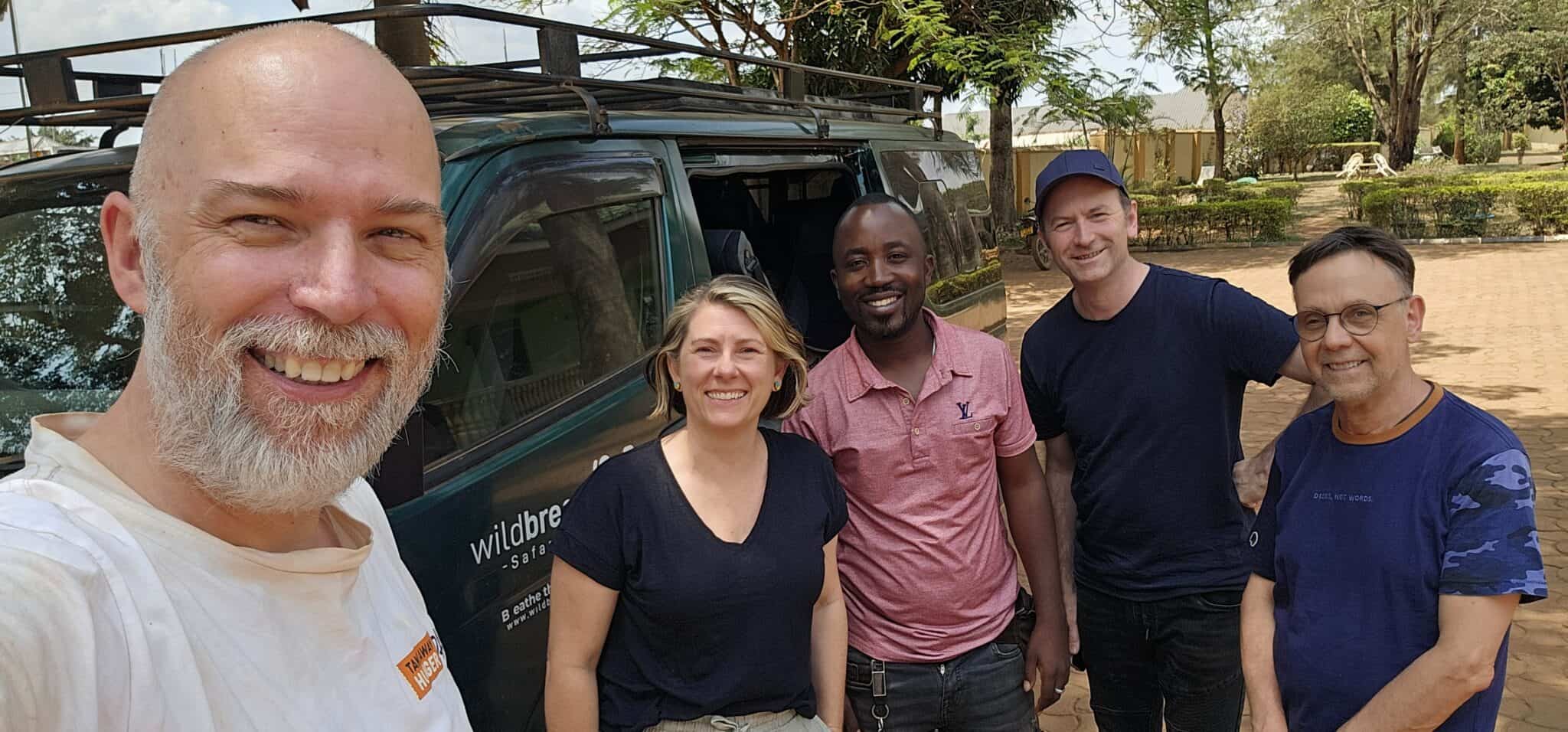 Fünf Personen stehen lächelnd im Freien vor einem grünen Lieferwagen, mit Bäumen und einem sonnigen Himmel im Hintergrund.